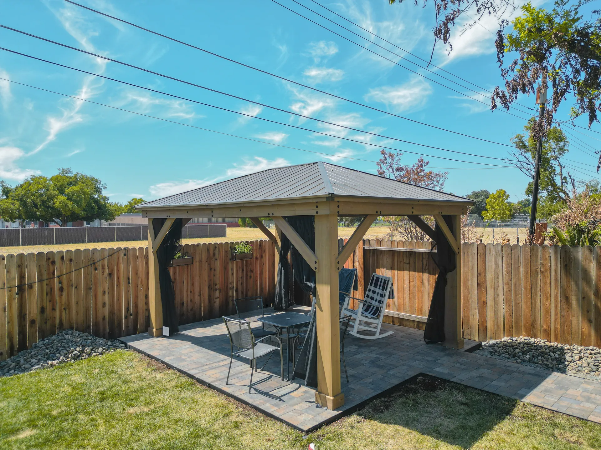 Pergola with paver patio, outdoor seating, and river rock landscaping in Sacramento backyard