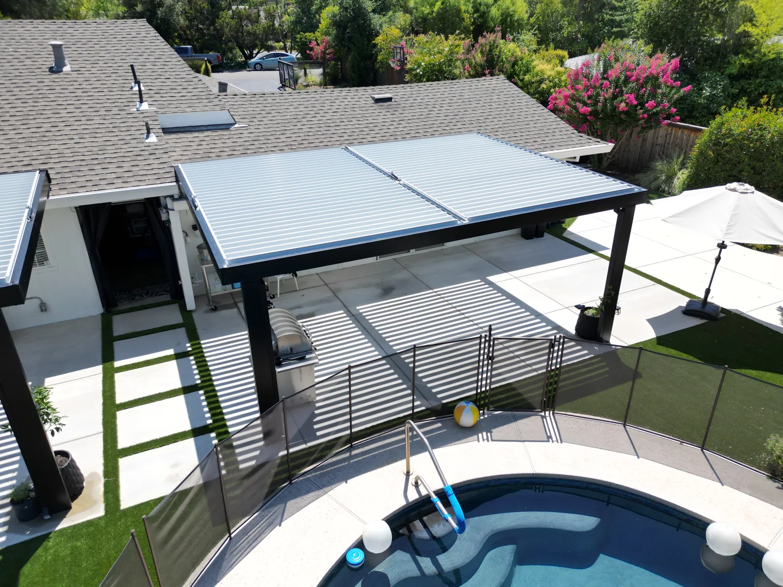 Close aerial of a louvered aluminum pergola with pool and safety fence below