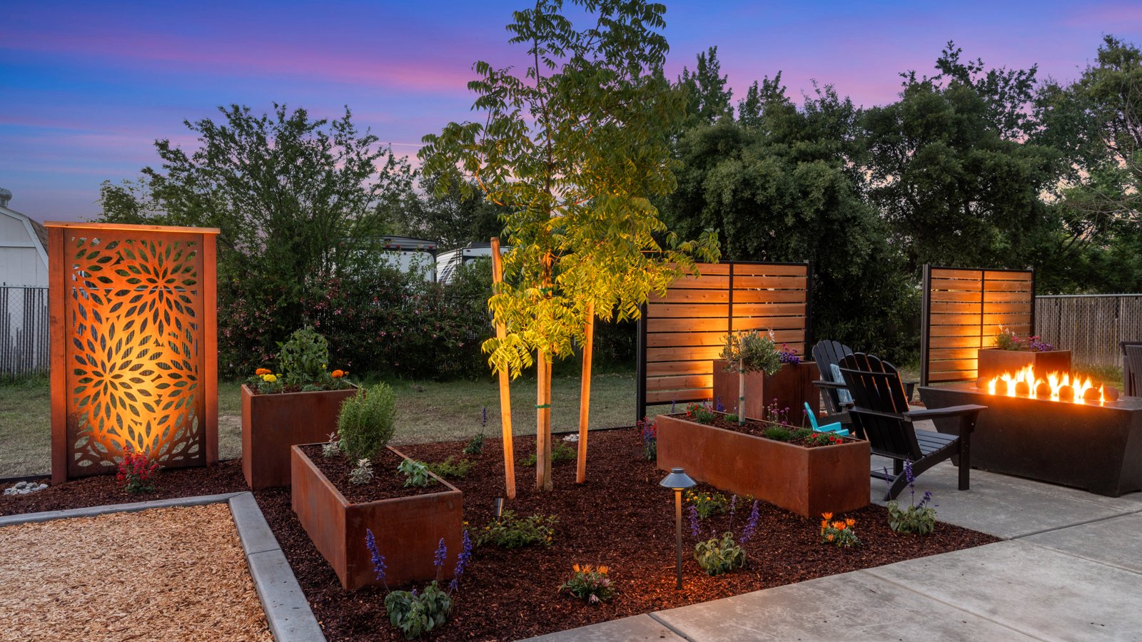 Backyard at dusk with glowing corten steel privacy screens and fire bowls by Stuteville Landscaping
